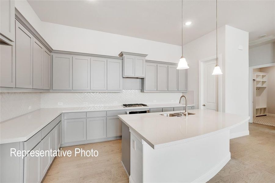 Kitchen with stainless steel gas cooktop, backsplash, an island with sink, hanging light fixtures, and sink