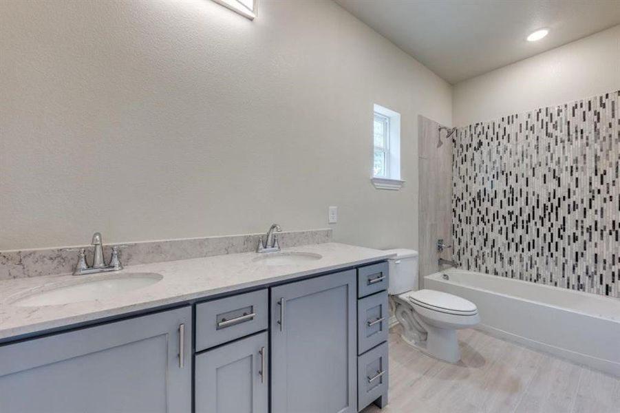 Full bathroom with double sink vanity, hardwood / wood-style floors, toilet, and tiled shower / bath combo