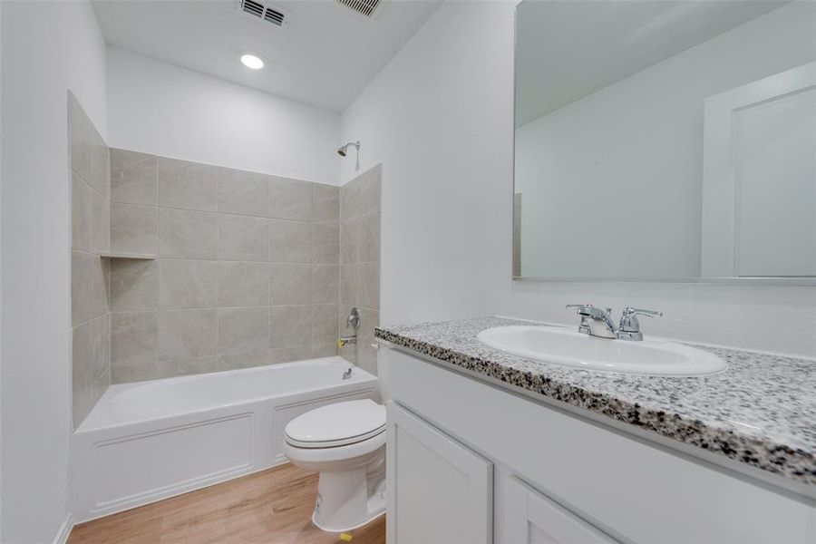 Full bathroom with vanity, tiled shower / bath combo, toilet, and wood-type flooring