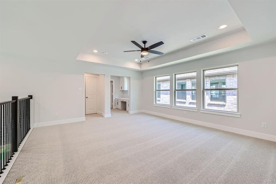 Unfurnished living room with a raised ceiling, light colored carpet, and ceiling fan