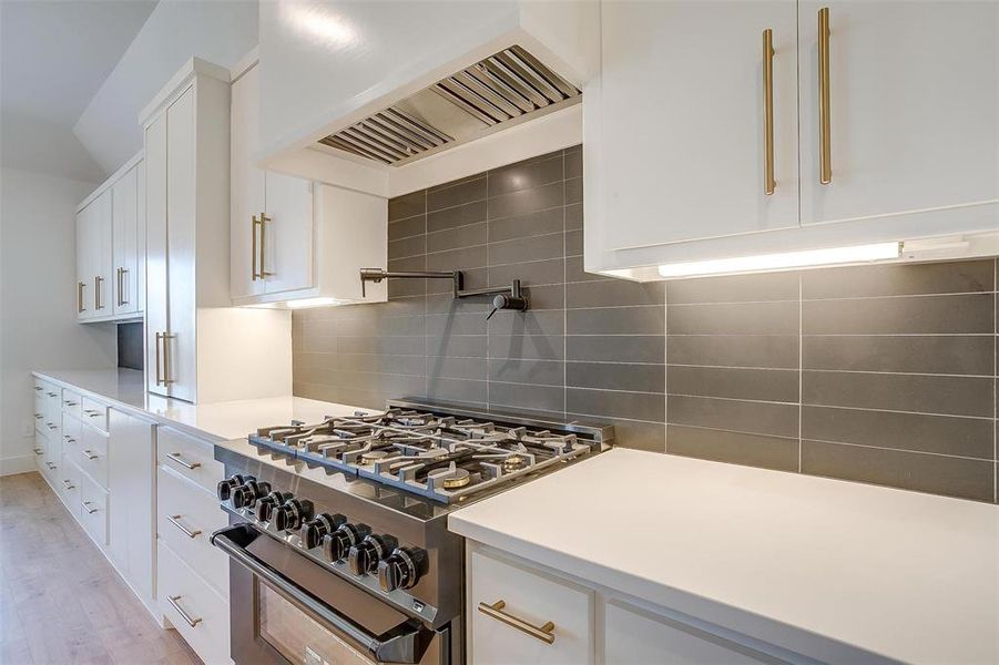 Kitchen with light wood-type flooring, range with two ovens, custom range hood, backsplash, and white cabinets
