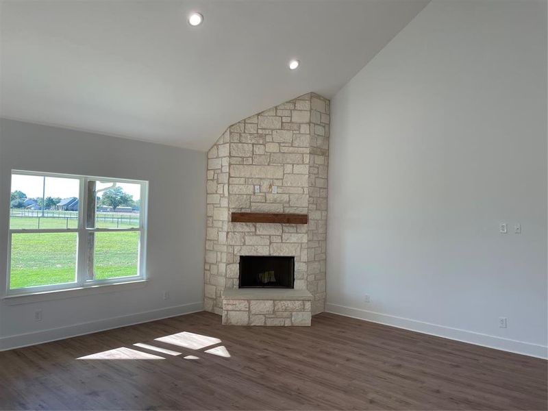 Unfurnished living room featuring dark hardwood / wood-style floors, a stone fireplace, and lofted ceiling