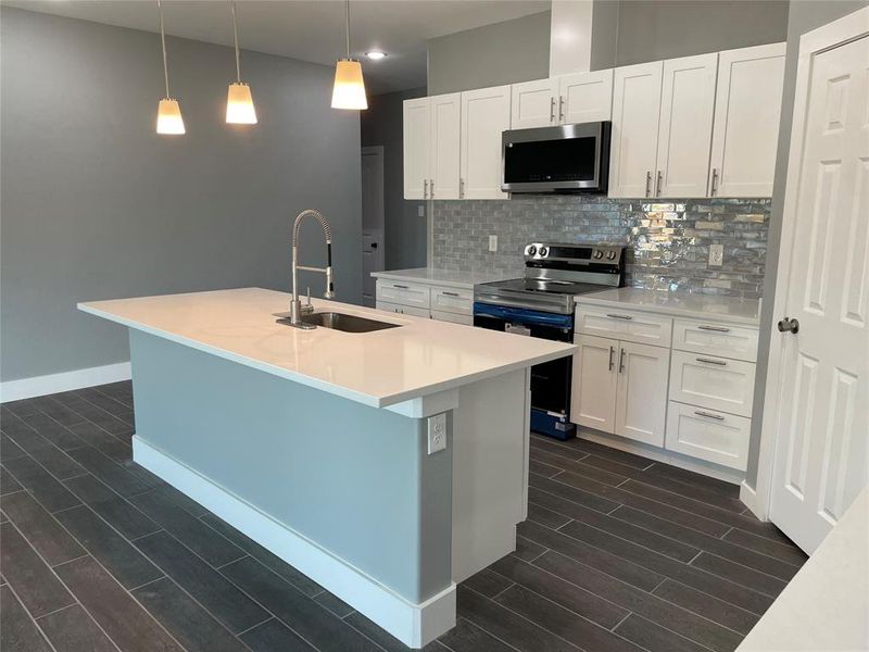 Kitchen with appliances with stainless steel finishes, white cabinets, decorative light fixtures, and a center island with sink