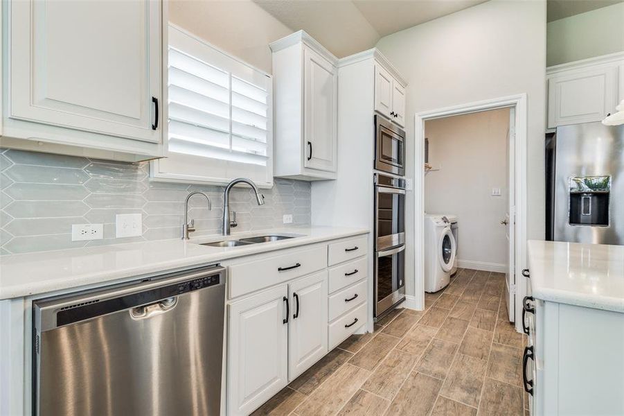 Kitchen with stainless steel appliances, sink, decorative backsplash, washer and dryer, and white cabinetry