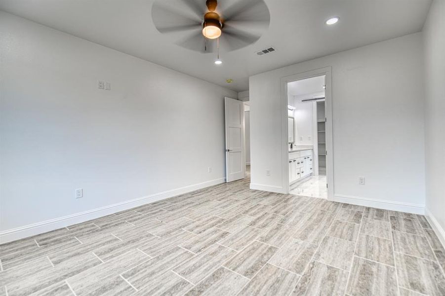 Unfurnished bedroom featuring a walk in closet, ensuite bathroom, light wood-type flooring, and ceiling fan