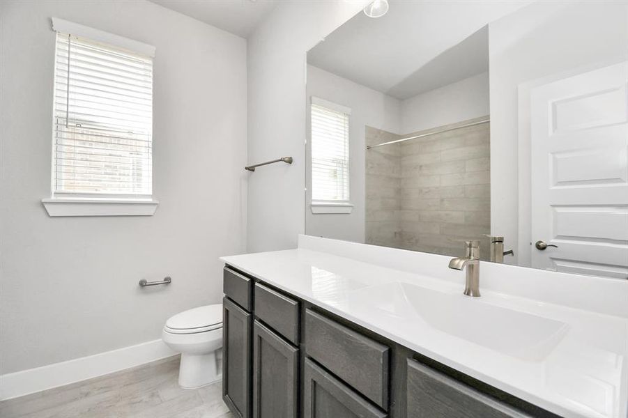 Experience sophistication in the secondary bathroom, where tile flooring complements a bath/shower combo with tile surround. Dark wood cabinets complete with a beautiful light countertop, enhances the space for a truly inviting ambiance.