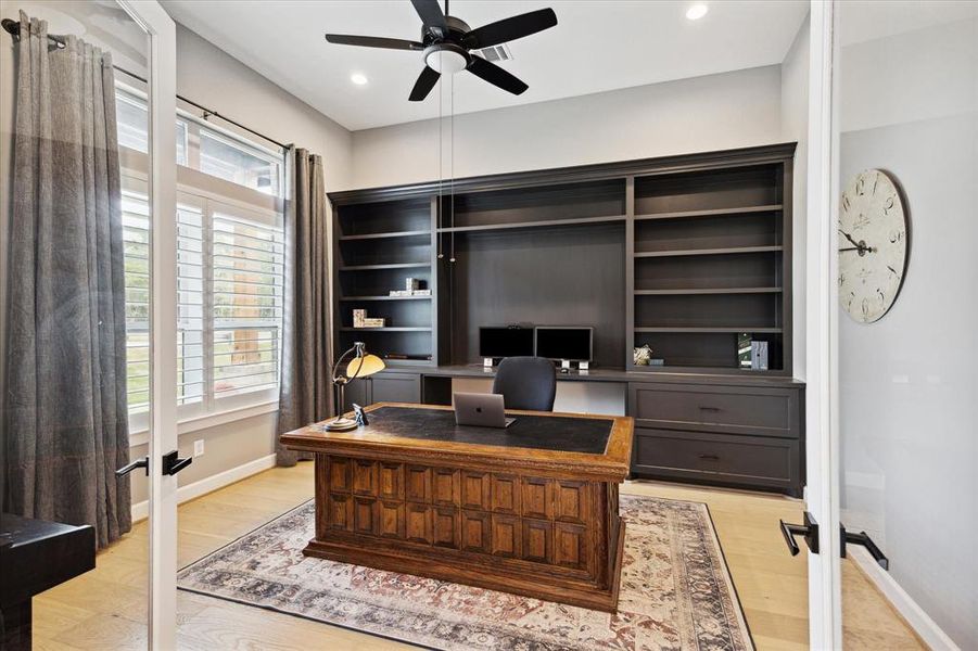Study with engineered wood floors, recessed lighting, ceiling fan, plantation shutters, and a built-in desk and cabinetry.