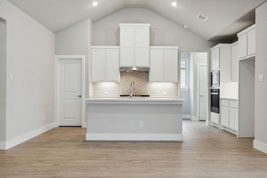Kitchen with an island with sink, light hardwood / wood-style floors, white cabinets, and stainless steel microwave