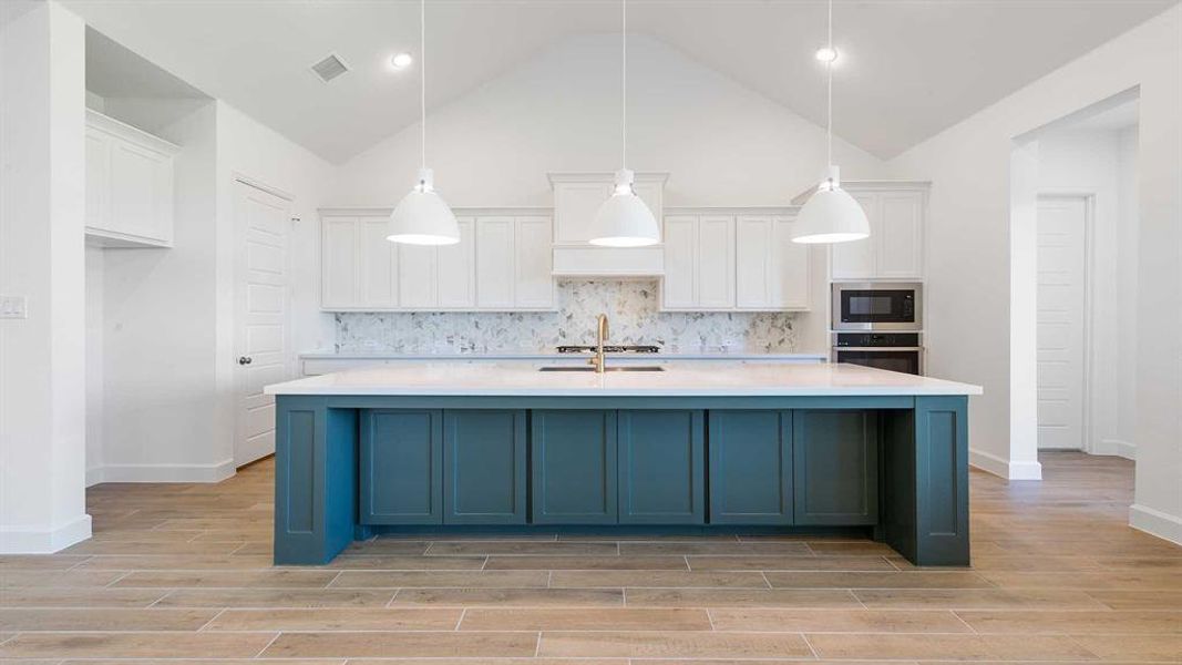 Kitchen with appliances with stainless steel finishes, hanging light fixtures, a kitchen island with sink, and white cabinets