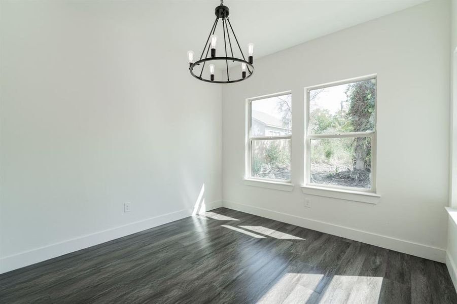 Empty room with dark hardwood / wood-style floors and an inviting chandelier