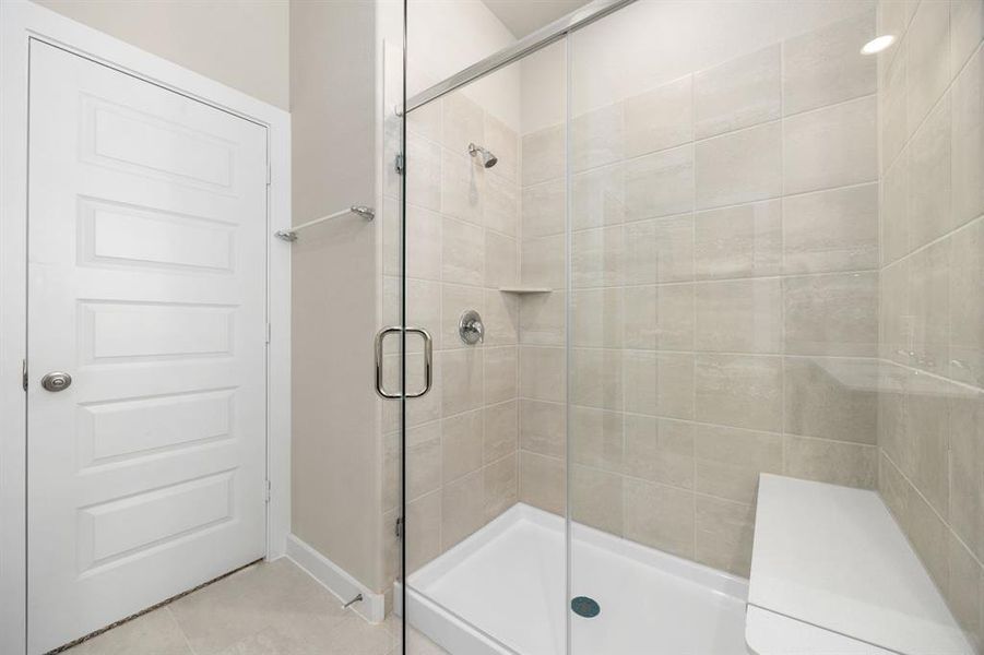 This additional view of the primary bath showcases an oversized walk-in shower with tile surround and a seating, perfect for soaking after a long day.