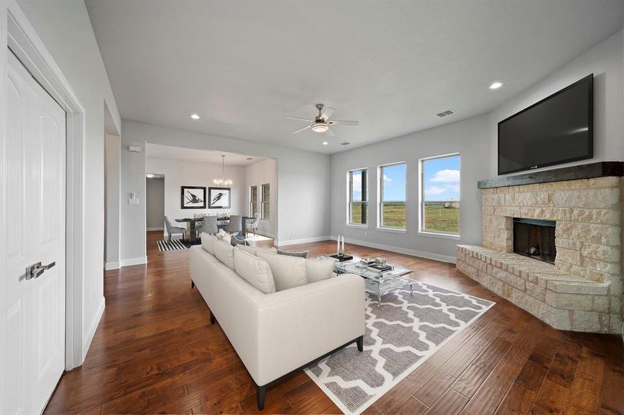 Living room featuring a stone fireplace, dark wood-type flooring, and ceiling fan with notable chandelier