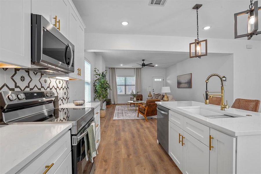 Kitchen featuring appliances with stainless steel finishes, sink, hardwood / wood-style floors, hanging light fixtures, and white cabinets