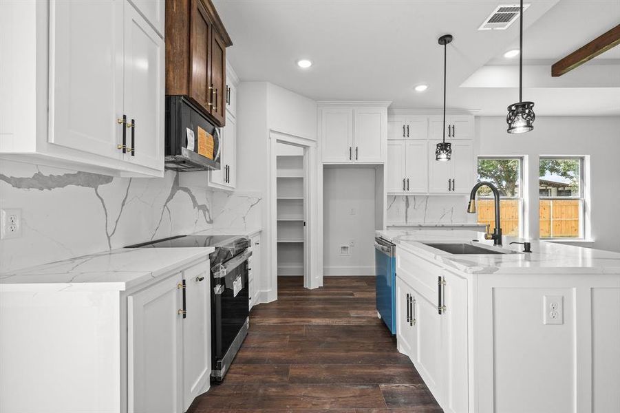 Kitchen with pendant lighting, an island with sink, stainless steel appliances, sink, and white cabinets