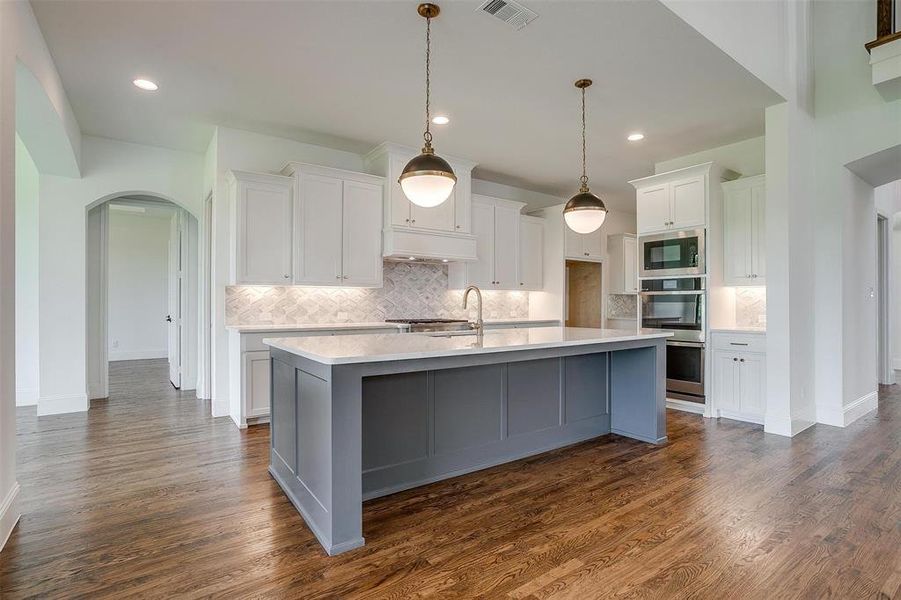 Kitchen with tasteful backsplash, an island with sink, dark hardwood / wood-style flooring, white cabinets, and appliances with stainless steel finishes