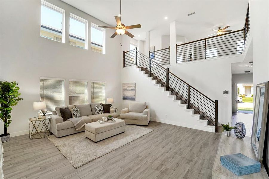 Living room featuring ceiling fan, a towering ceiling, and light hardwood / wood-style floors