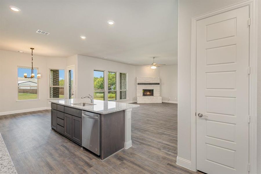 Kitchen with light stone counters, pendant lighting, dishwasher, a fireplace, and ceiling fan with notable chandelier