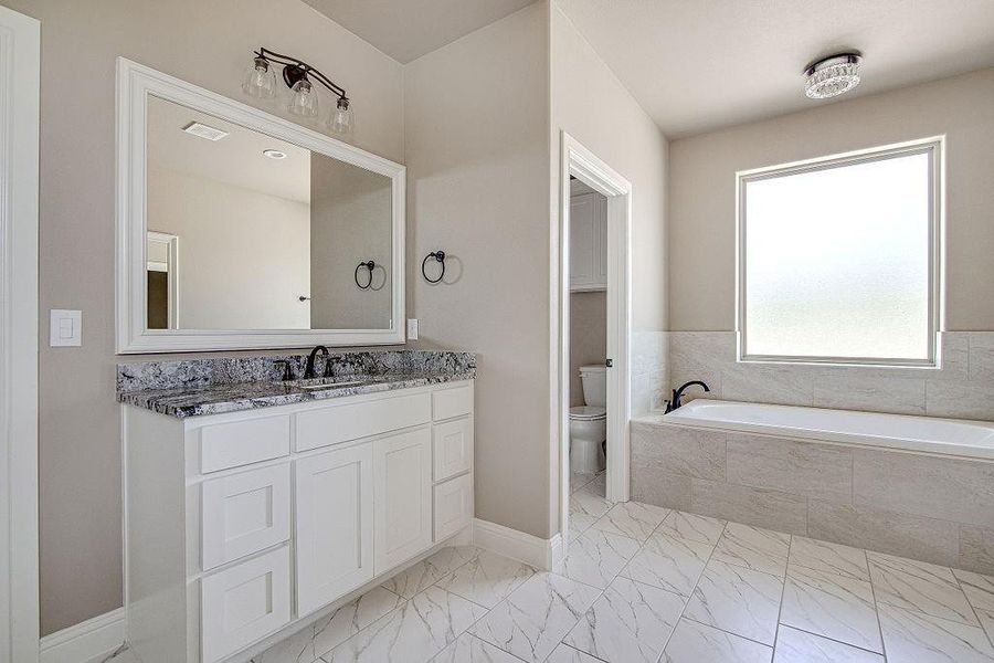 Bathroom with vanity, toilet, tile patterned flooring, and a relaxing tiled tub