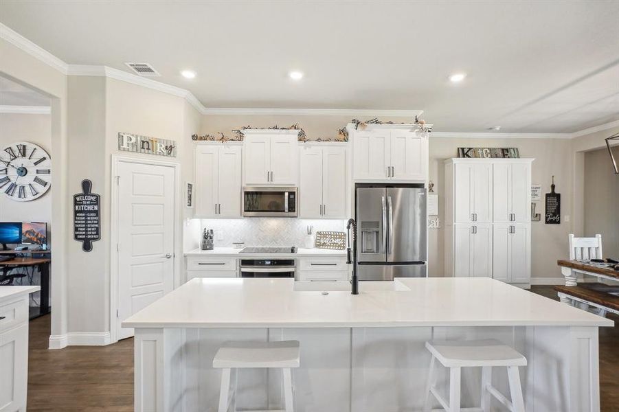 Kitchen featuring an island with sink, white cabinets, appliances with stainless steel finishes, and a kitchen bar