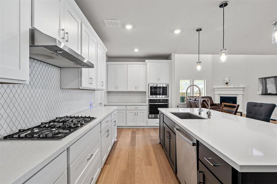 Kitchen featuring appliances with stainless steel finishes, white cabinets, decorative light fixtures, a kitchen island with sink, and sink