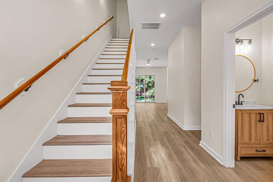 First floor entry way with powder room to the right, stained wood accents on the stairway and main living space beyond.