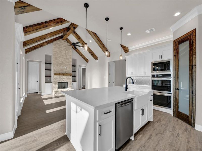 Kitchen with appliances with stainless steel finishes, a stone fireplace, an island with sink, white cabinetry, and ceiling fan