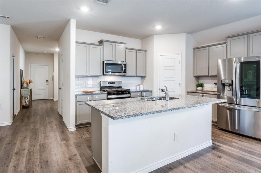 Kitchen with wood-type flooring, sink, stainless steel appliances, light stone counters, and a kitchen island with sink