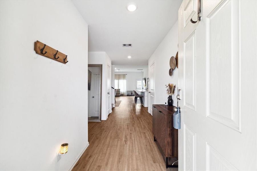 This photo shows a bright and airy hallway , leading into an open-plan area with natural light. The walls are painted white giving the space a clean and modern feel.