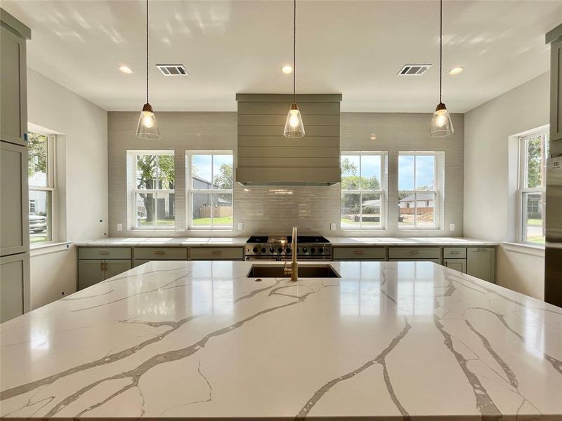 Kitchen with light stone counters, hanging light fixtures, and plenty of natural light