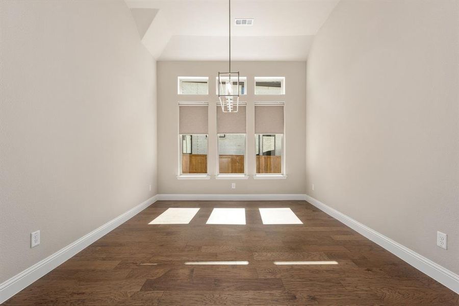 Unfurnished dining area featuring an inviting chandelier, lofted ceiling, and dark hardwood / wood-style floors