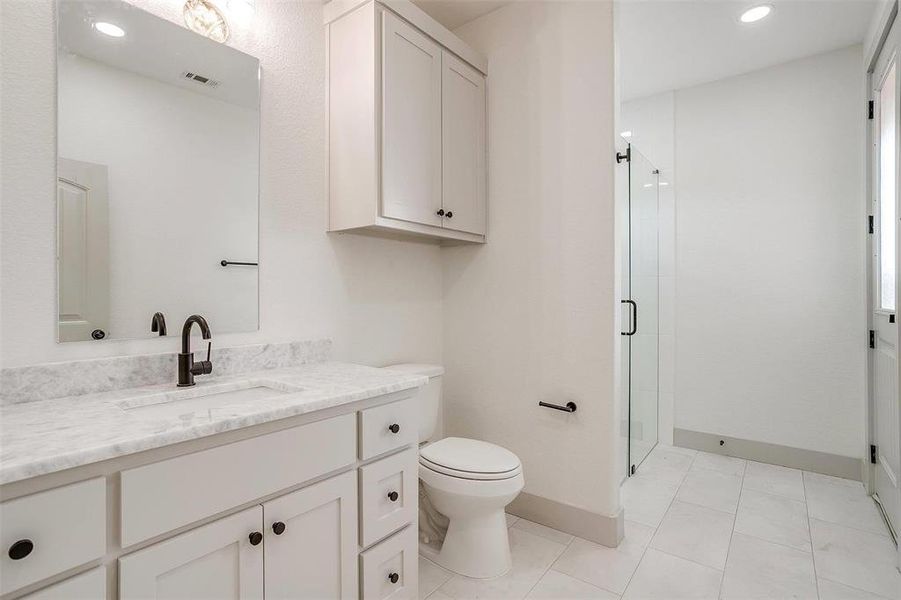 Bathroom with a shower with shower door, tile patterned flooring, toilet, and vanity