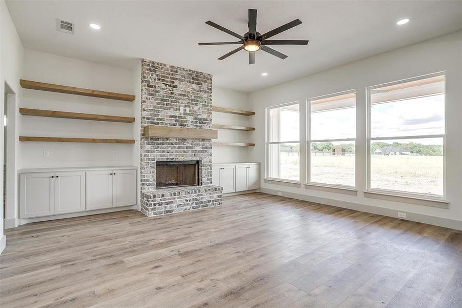 Unfurnished living room with light wood-type flooring, ceiling fan, and a fireplace