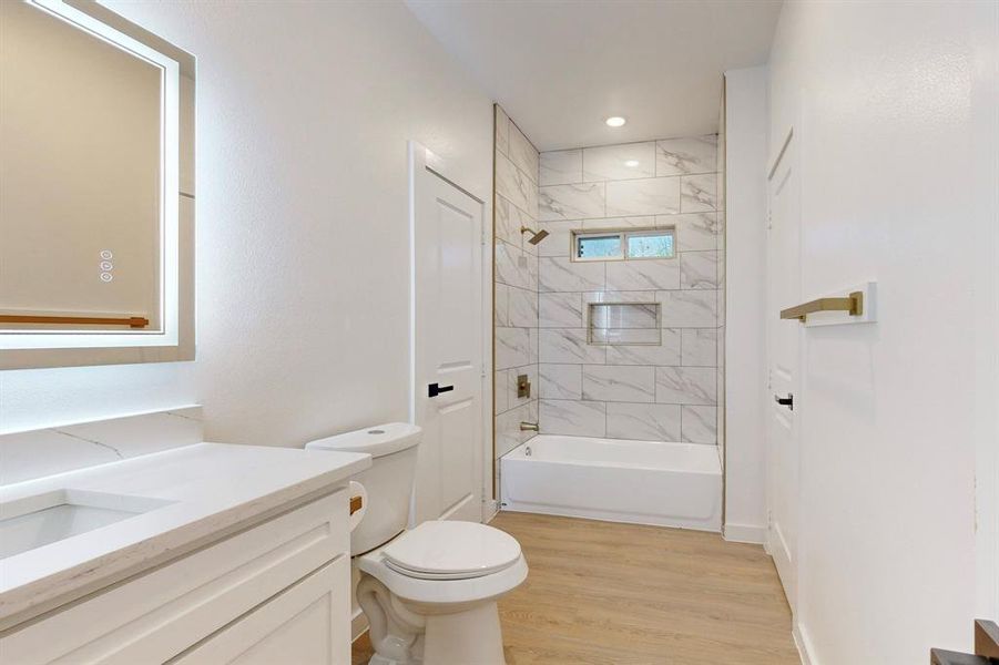 Full bathroom featuring toilet, vanity, tiled shower / bath combo, and hardwood / wood-style flooring