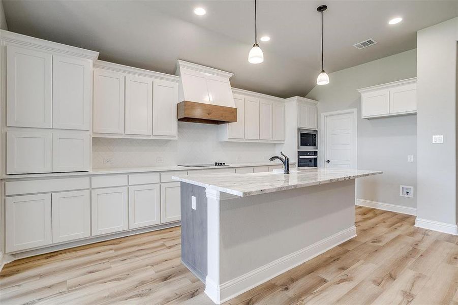 Kitchen featuring premium range hood, black appliances, white cabinets, an island with sink, and light hardwood / wood-style floors