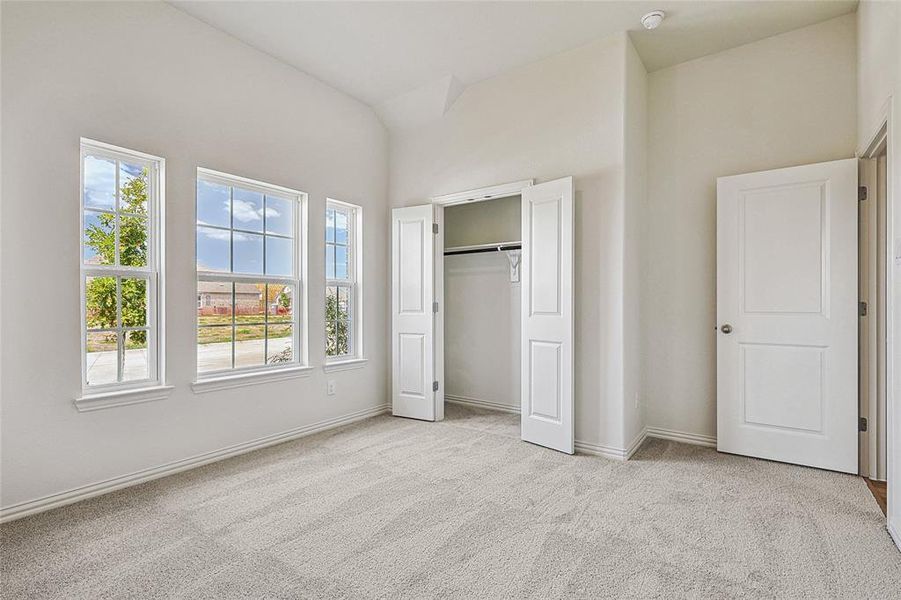 Unfurnished bedroom featuring a closet, light carpet, high vaulted ceiling, and multiple windows