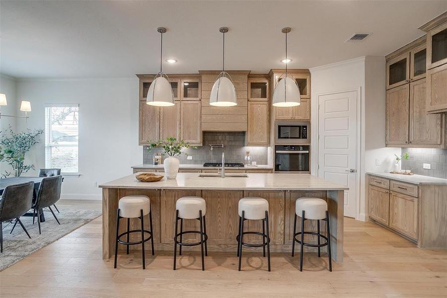 Kitchen featuring light hardwood flooring, a kitchen island with leathered Quartzite countertops, farm sink, natural stain custom cabinetry with soft close drawers and cabinets.