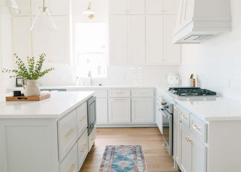 Kitchen with light hardwood / wood-style floors, hanging light fixtures, white cabinetry, backsplash, and custom exhaust hood