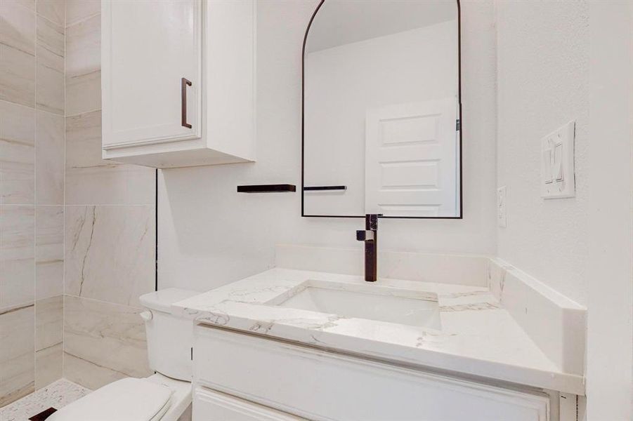 Bathroom featuring tiled shower, vanity, and toilet