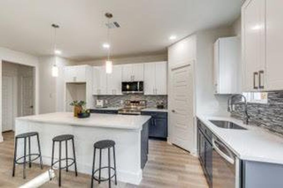 Kitchen with white cabinetry, light hardwood / wood-style flooring, tasteful backsplash, a center island, and appliances with stainless steel finishes