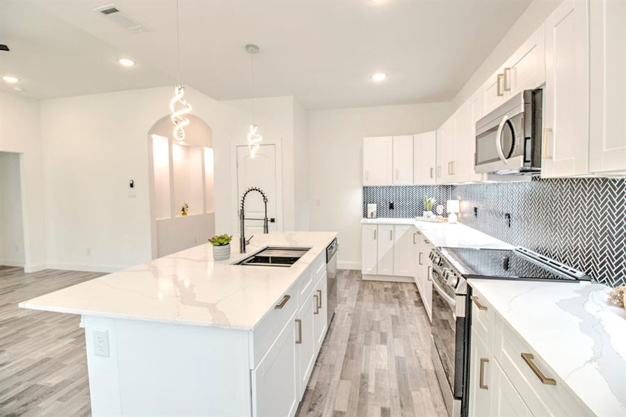 Kitchen featuring sink, appliances with stainless steel finishes, light hardwood / wood-style flooring, and an island with sink