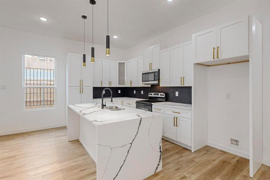 Kitchen with light stone counters, sink, an island with sink, white cabinetry, and appliances with stainless steel finishes