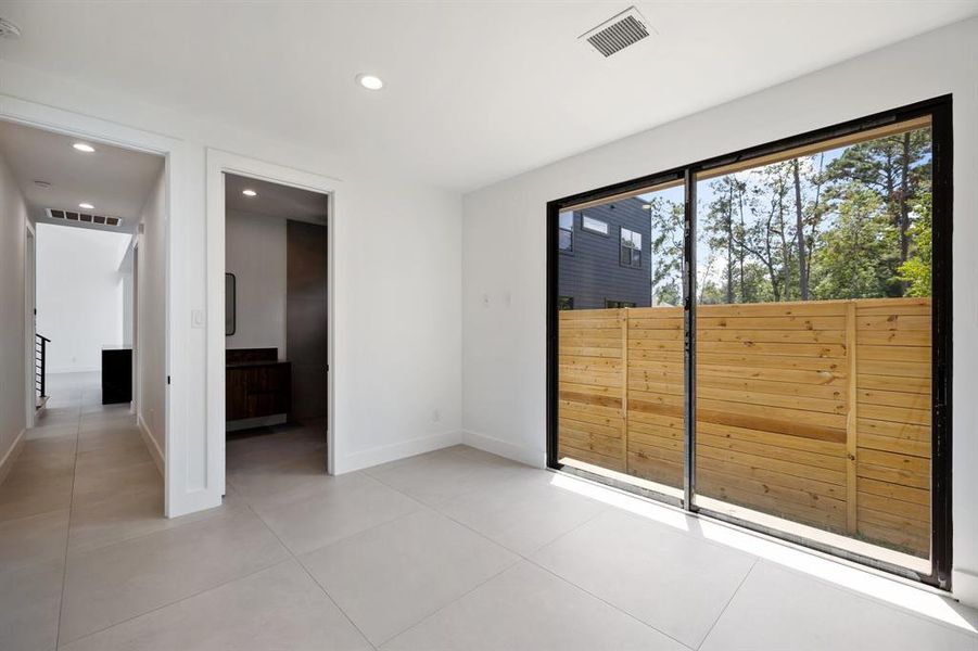 This is a bright, modern space with large sliding glass doors leading to an outdoor area, featuring a wooden privacy fence. The room has a clean, minimalist design with light porcelain tile flooring and white walls. It appears to be a blank canvas ready for personalization.