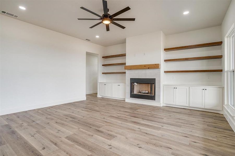 Unfurnished living room with light wood-type flooring, ceiling fan, and a tile fireplace