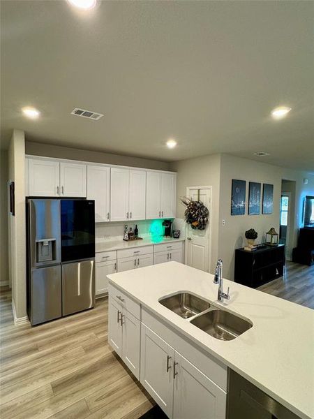 Kitchen with stainless steel refrigerator with ice dispenser, light wood-type flooring, white cabinetry, and sink