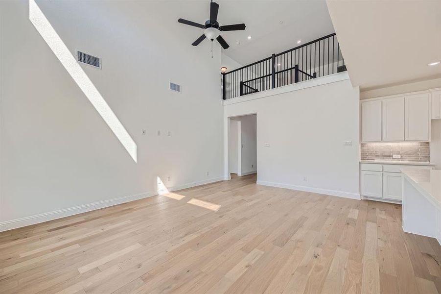 Unfurnished living room with light wood-type flooring, a high ceiling, ceiling fan, and a skylight