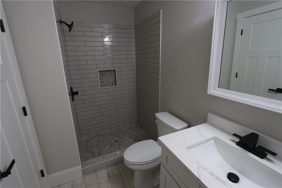 Bathroom with toilet, tile flooring, a tile shower, and vanity