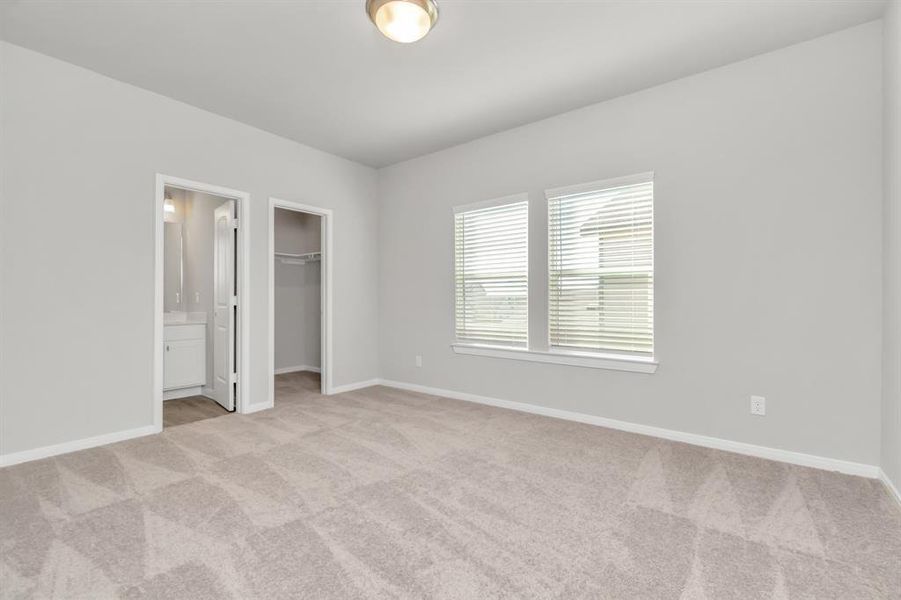 This spacious secondary bedroom offers ample natural light, plush carpeting, and direct access to an en-suite bathroom and walk-in closet. The room’s neutral tones provide a calming atmosphere, making it an ideal space for guests or family members. The thoughtful layout ensures privacy and convenience, with easy access to storage and personal amenities. **This image is from another Saratoga Home with similar floor plan and finishes, not the June floorplan.**