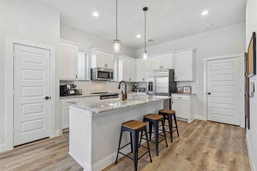 Kitchen with light wood-type flooring, white cabinets, an island with sink, appliances with stainless steel finishes, and decorative backsplash