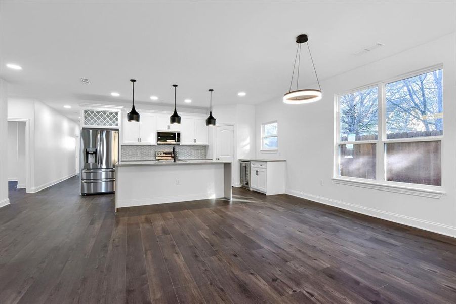 Kitchen with dark hardwood / wood-style floors, decorative light fixtures, an island with sink, stainless steel appliances, and white cabinetry