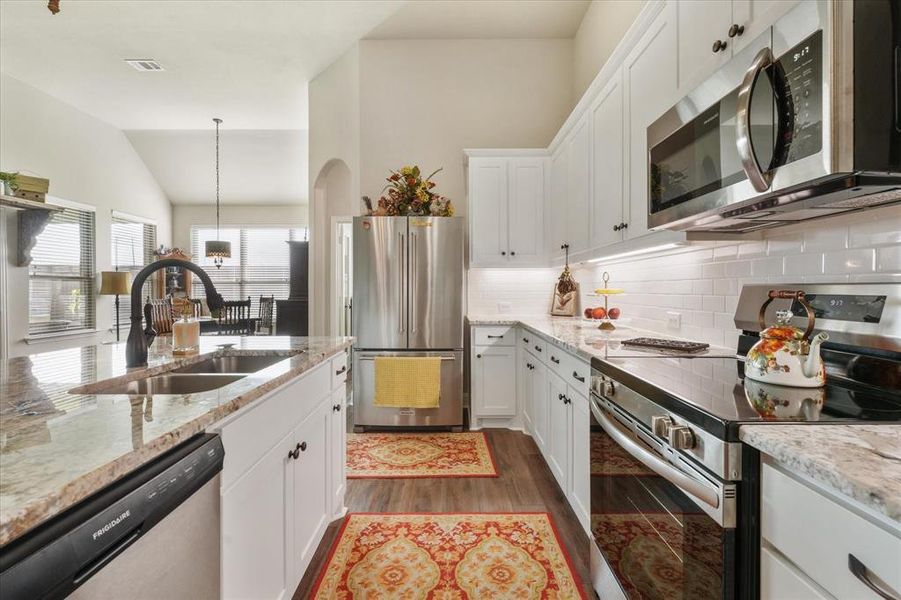 Kitchen with lofted ceiling, tasteful backsplash, white cabinets, dark hardwood / wood-style floors, and stainless steel appliances